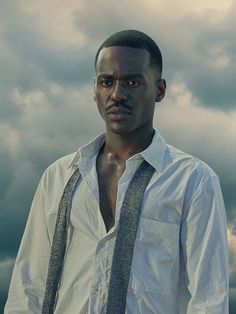 a man in white shirt and tie standing under cloudy sky