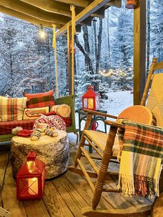 a porch with rocking chairs and blankets on the deck in front of snowy trees at night