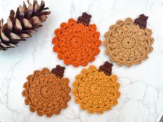 three crocheted coasters sitting next to a pine cone on a marble surface