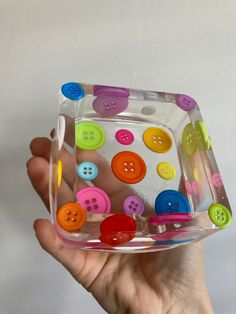 a hand holding a clear container filled with colorful buttons