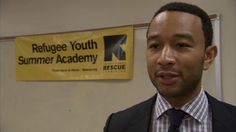 a man wearing a suit and tie standing in front of a sign that reads refuge youth summer academy