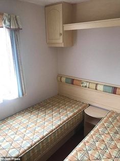 two twin beds in a small room with cupboards on the wall and window behind them