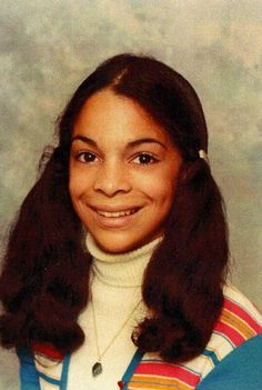 an old photo of a woman with long dark hair and wearing a striped sweater, smiling at the camera