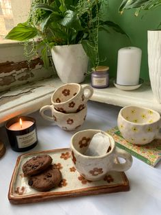 two mugs with cookies on a tray next to a candle and potted plant