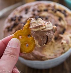 a hand holding a cracker with chocolate chip cookie dip in it and other desserts on the table