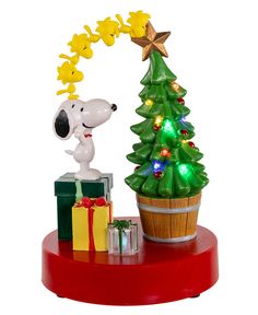 a snoopy christmas tree with presents under it and a dog figurine next to it