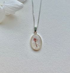 a dandelion flower in a round glass pendant on a silver chain with a white background