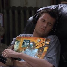 a man laying in a chair with headphones on and holding a book to his face