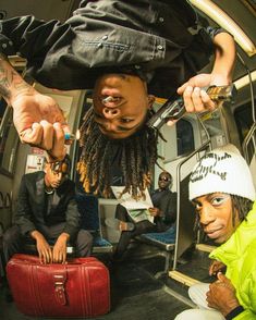 two men sitting on a bus with their hands in the air and one holding a red suitcase