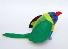 a small stuffed bird sitting on top of a white table next to a red, yellow and green parrot