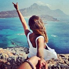 a woman sitting on top of a rock next to the ocean with her arms in the air