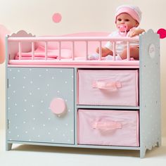 a baby doll sitting on top of a pink and gray crib with polka dots