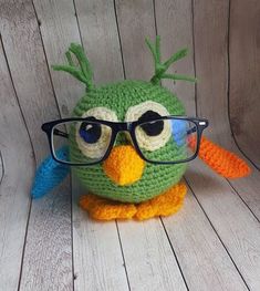 a crocheted green bird with glasses on it's head sitting on a wooden floor