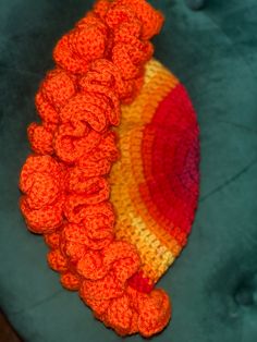 an orange crocheted hat sitting on top of a blue chair next to a green cushion