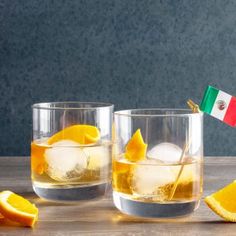 two glasses filled with ice and orange slices next to an italian flag on the table