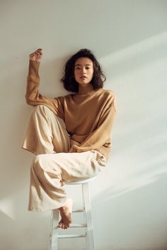 a woman sitting on top of a stool next to a white wall with her legs crossed