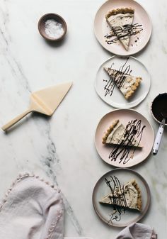 there are four slices of cheesecake on the plates with chocolate drizzled on them