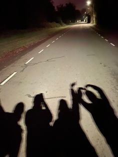 three people standing in the middle of a road at night with their shadows on the ground