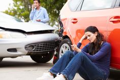 a woman sitting on the ground next to a car with her head in her hand