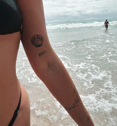 a woman with a tattoo on her arm stands in the water at the beach while another person swims in the background