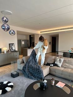 a woman standing on top of a couch in a living room next to a cat