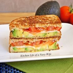 two sandwiches are stacked on top of each other with tomatoes and avocado in the background