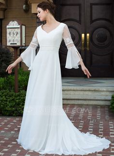 a woman standing in front of a door wearing a white dress with bell sleeves and an open back