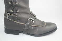 Grey boots make an excellent accompaniment to almost any outfit. Metal studs run vertically up the side with leather laces. Together the leather strap around the arch gives and tan trim around the base of your toes gives these boots an equestrian feel with a unique tailored twist. Approx: 1/4" heel Shiny studs add edgy style to these tall leather boots from J. Litvack. Featuring a round toe, dual adjustable ankle straps with side buckle closure, and leather weaving throughout the side studs. Leather Moto Boots With Grommets For Fall, Leather Moto Boots With Silver Studs For Fall, Leather Ankle Moto Boots With Lacing, Leather Boots With Rivets And Snip Toe, Western Leather Boots With Rivets, Studded Leather Boots With Almond Toe, Leather Lace-up Boots With Buckle Closure, Leather Lace-up Boots With Rivets, Leather Boots With Silver Studs And Snip Toe