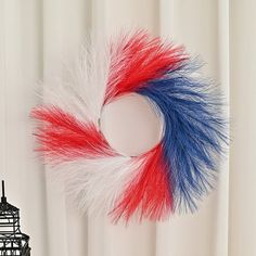 a red, white and blue feather wreath hanging on a wall next to a window