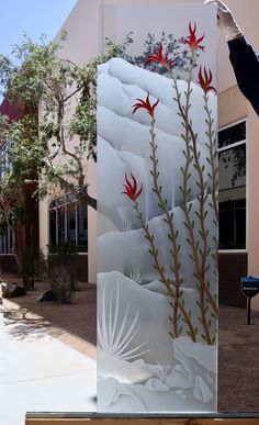 a person holding up a frosted glass panel with red flowers and leaves on it