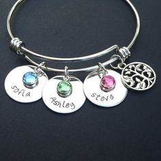 three personalized charms are attached to a silver bang bracelet with the names and date on it