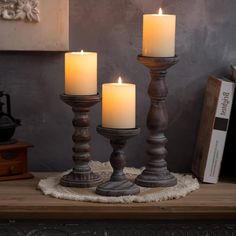 three candles sitting on top of a wooden table next to a book and some books