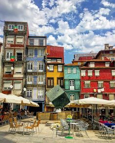 an outdoor cafe with tables and umbrellas in front of colorful buildings on a cloudy day