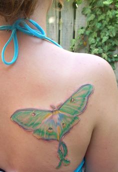 a butterfly tattoo on the back of a woman's upper body, with blue ribbon around her neck