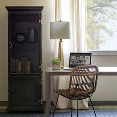 a desk with a chair and a bookcase in front of a window next to a lamp