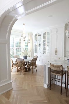 an archway leads into a dining room and kitchen with white walls, wood floors and wooden chairs