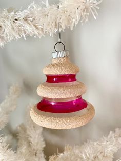 a pink and white ornament hanging from a christmas tree