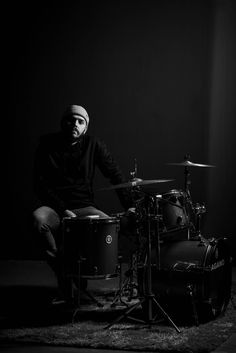 a man sitting behind a drum set on top of a carpeted floor in front of a black wall