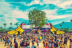 a large group of people standing in front of a yellow tent on top of a dirt field