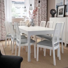 a white table and chairs in a room with flowers on the window curtained windowsill