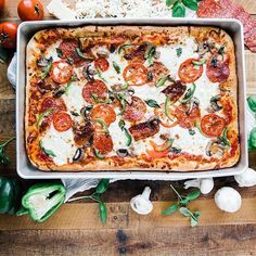 a square pizza sitting on top of a pan covered in cheese and toppings next to vegetables