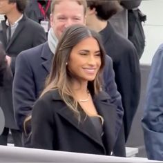 a woman standing in front of a crowd wearing a black jacket and white dress shirt