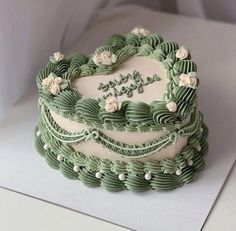 a heart shaped cake with green frosting and white flowers on the top that says happy birthday