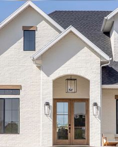 the front entrance to a white brick house with two large doors and windows on each side