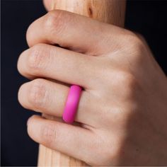 a person's hand with a pink ring on their finger and a wooden stick in the background