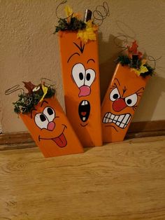 three orange vases with faces painted on them sitting on a wooden floor next to a wall