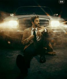 a man sitting on the ground in front of a car