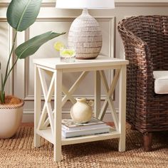 a white table with a lamp on it next to a wicker chair and potted plant