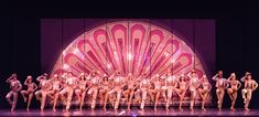 a group of people sitting on top of a stage next to each other in front of a giant fan