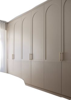 a white bed sitting under a window next to a tall cabinet with doors on it